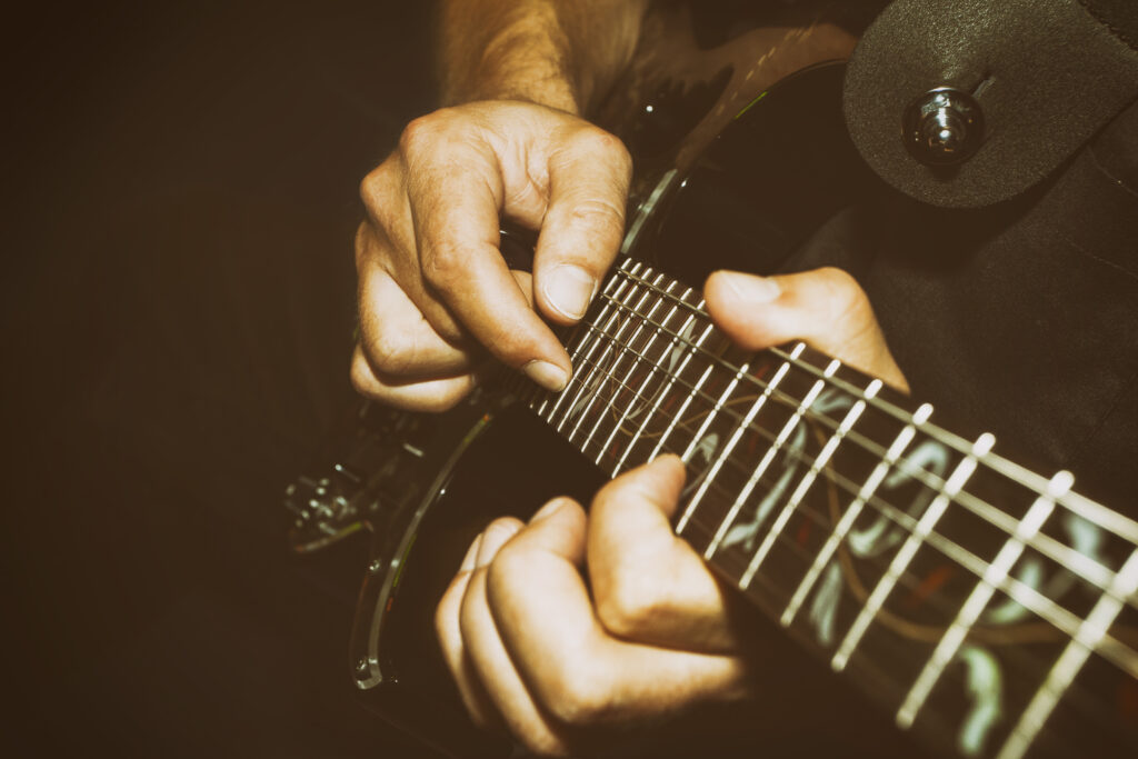 Closeup of a guitar (strings and frets) being played by a man.
